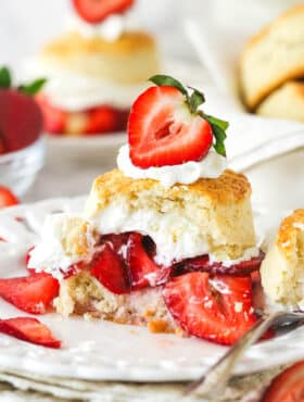Strawberry shortcake on a plate with a couple of bites taken out of it.