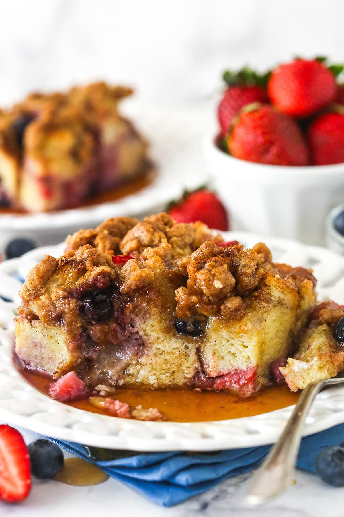 A slice of berry French toast casserole on a plate with a couple of bites taken out of it.