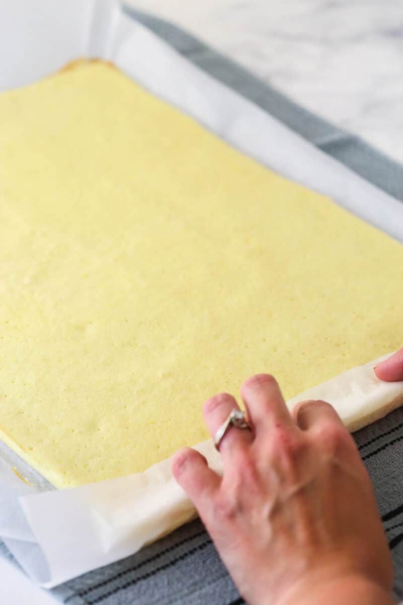 baked cake and parchment paper sitting on the counter on a hand towel as it starts to be rolled