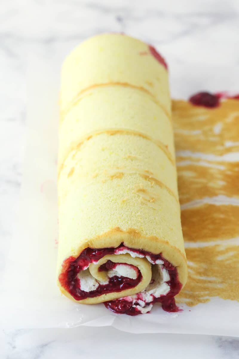cake roll sitting on parchment paper on the counter after being filling and rolled back up