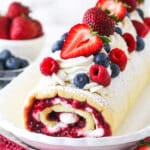 decorated Berry Vanilla Cake Roll on a white platter with berries in the background