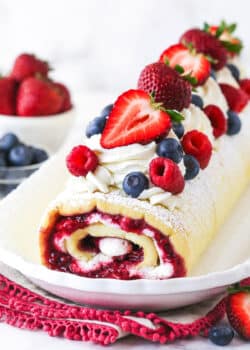 decorated Berry Vanilla Cake Roll on a white platter with berries in the background