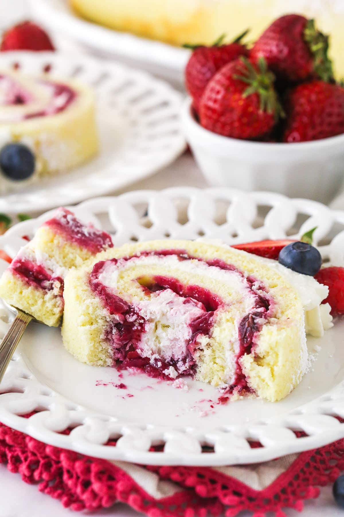 slice of Berry Vanilla Cake Roll on a white plate with a bite taken out