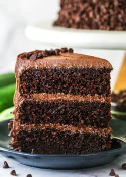 A slice of chocolate zucchini cake upright on a plate.