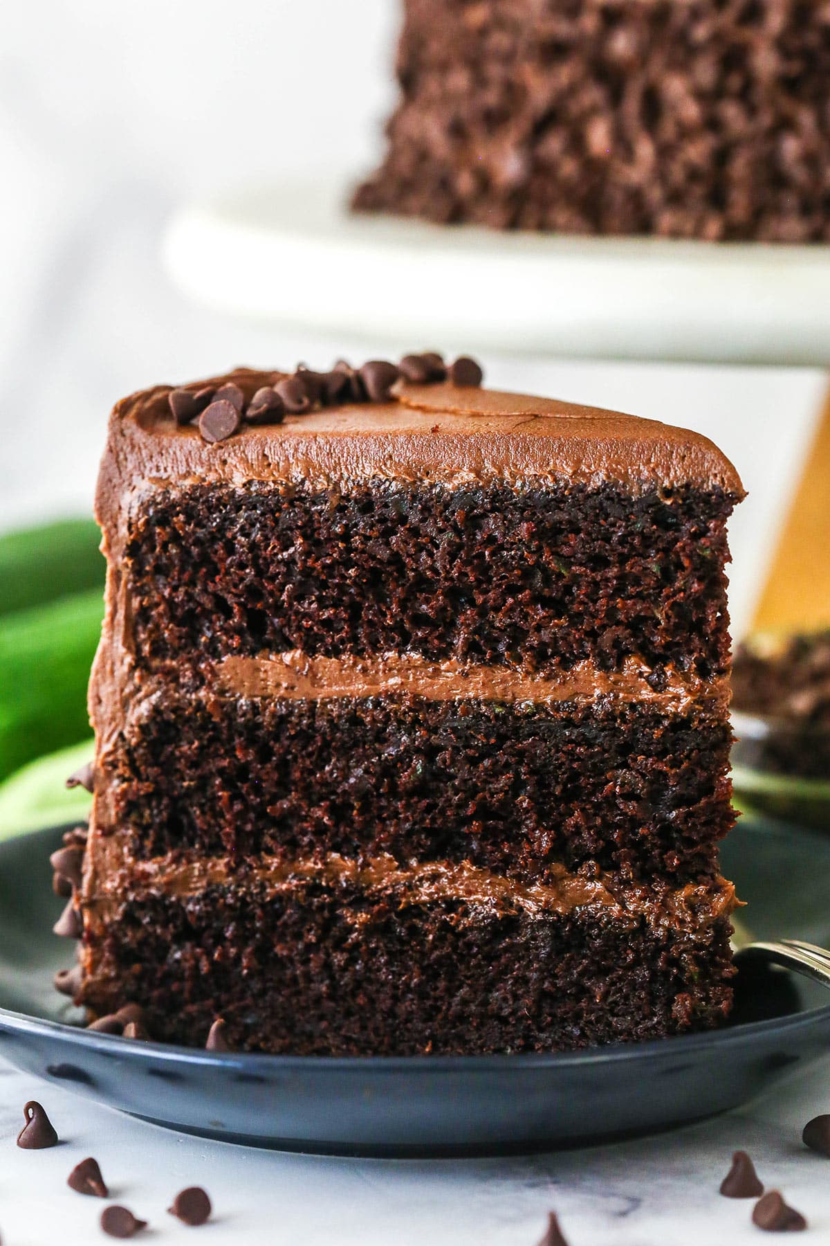 A slice of chocolate zucchini cake upright on a plate.