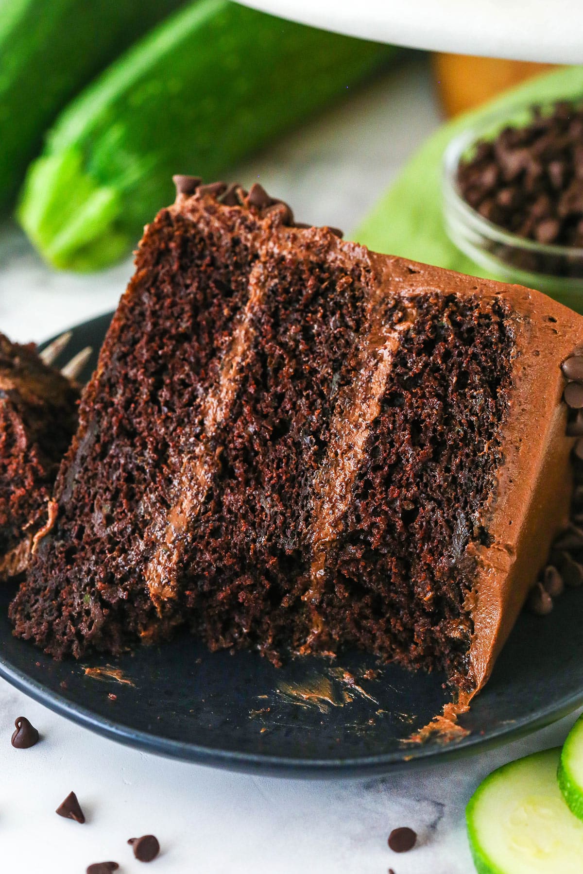 A slice of chocolate zucchini cake on a plate with a bite taken out of it.