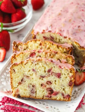 A loaf of strawberry bread with 3 slices leaning up against it.