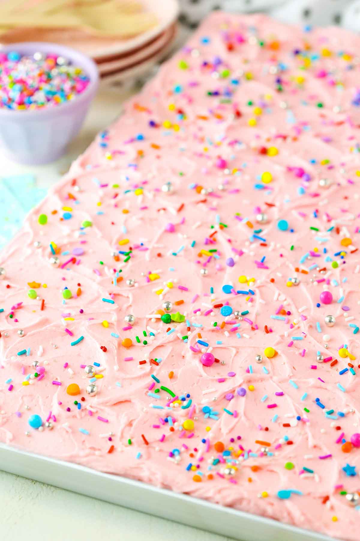 A full Vanilla Sheet Cake next to a bowl of sprinkles
