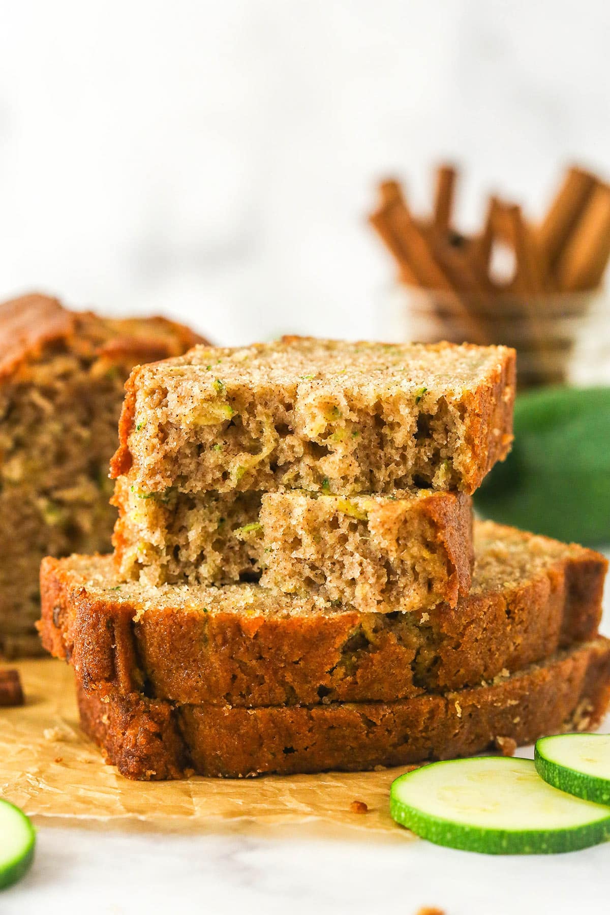 Sliced of zucchini bread stacked on top of each other. The top slice is torn in half.