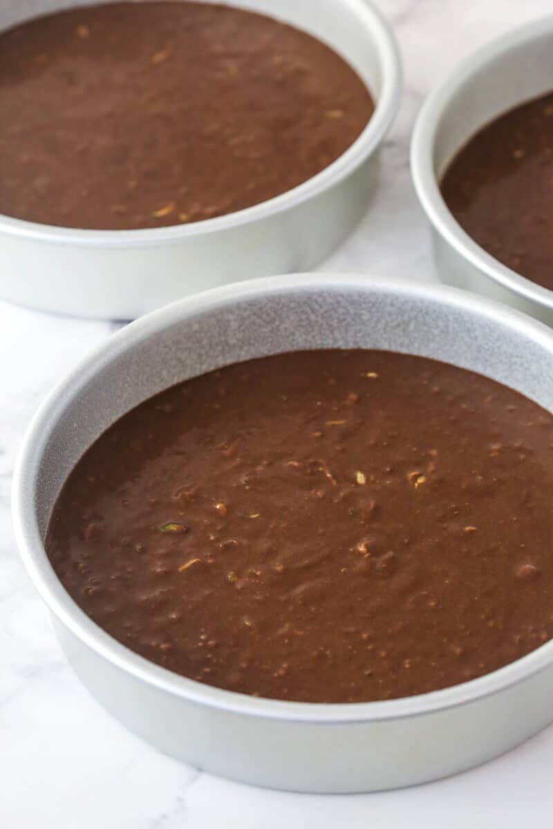 Chocolate zucchini cake batter divided between 3 cake pans.