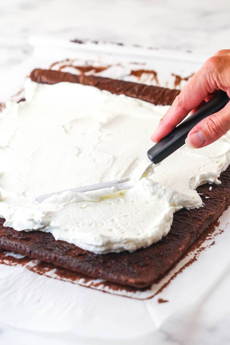 Whipped cream filling being spread on chocolate cake