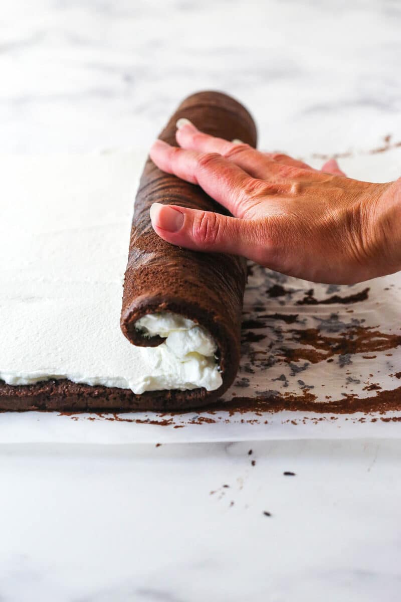 A hand rolling a Swiss roll cake over the filling