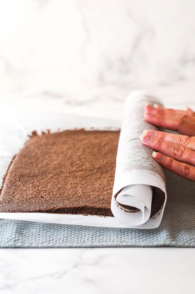 Fingers rolling a chocolate roll cake in parchment paper