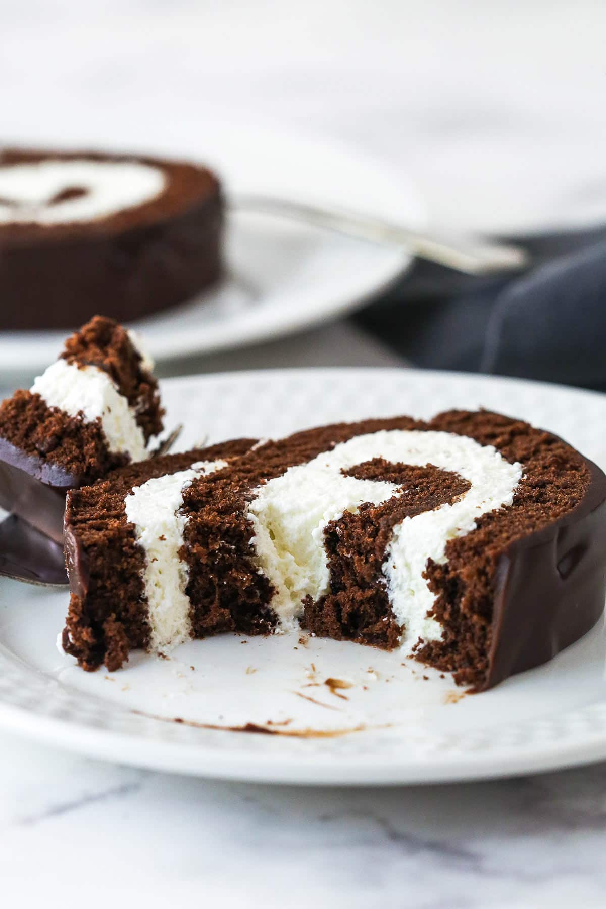 A slice of chocolate Swiss roll with a bite missing on a plate