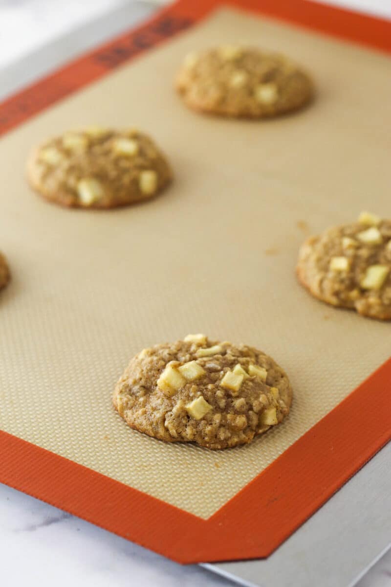 Baked apple cinnamon oatmeal cookies on a baking mat.