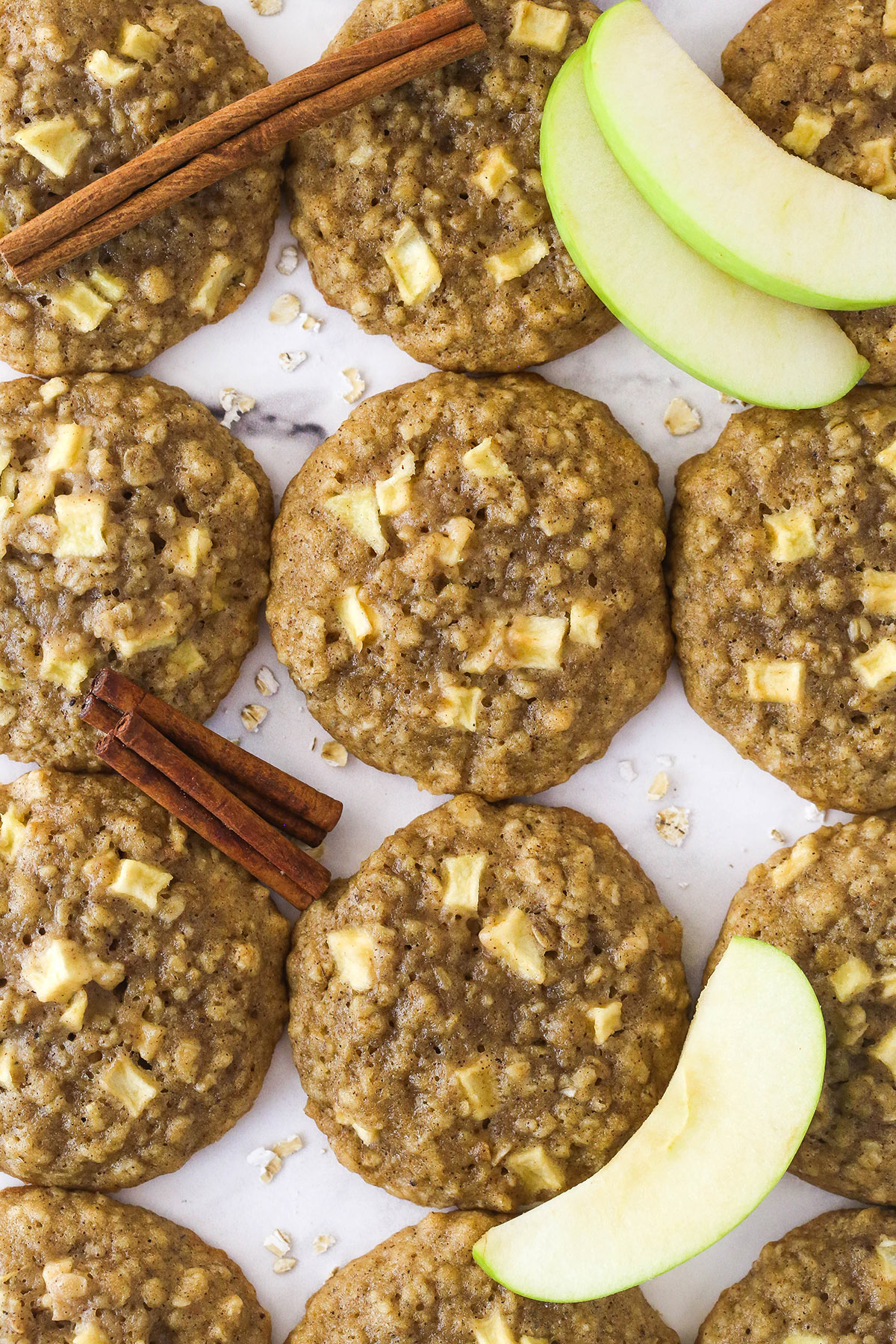 Top view of cooked Apple Cinnamon Oatmeal Cookies next to cinnamon and apple slices.