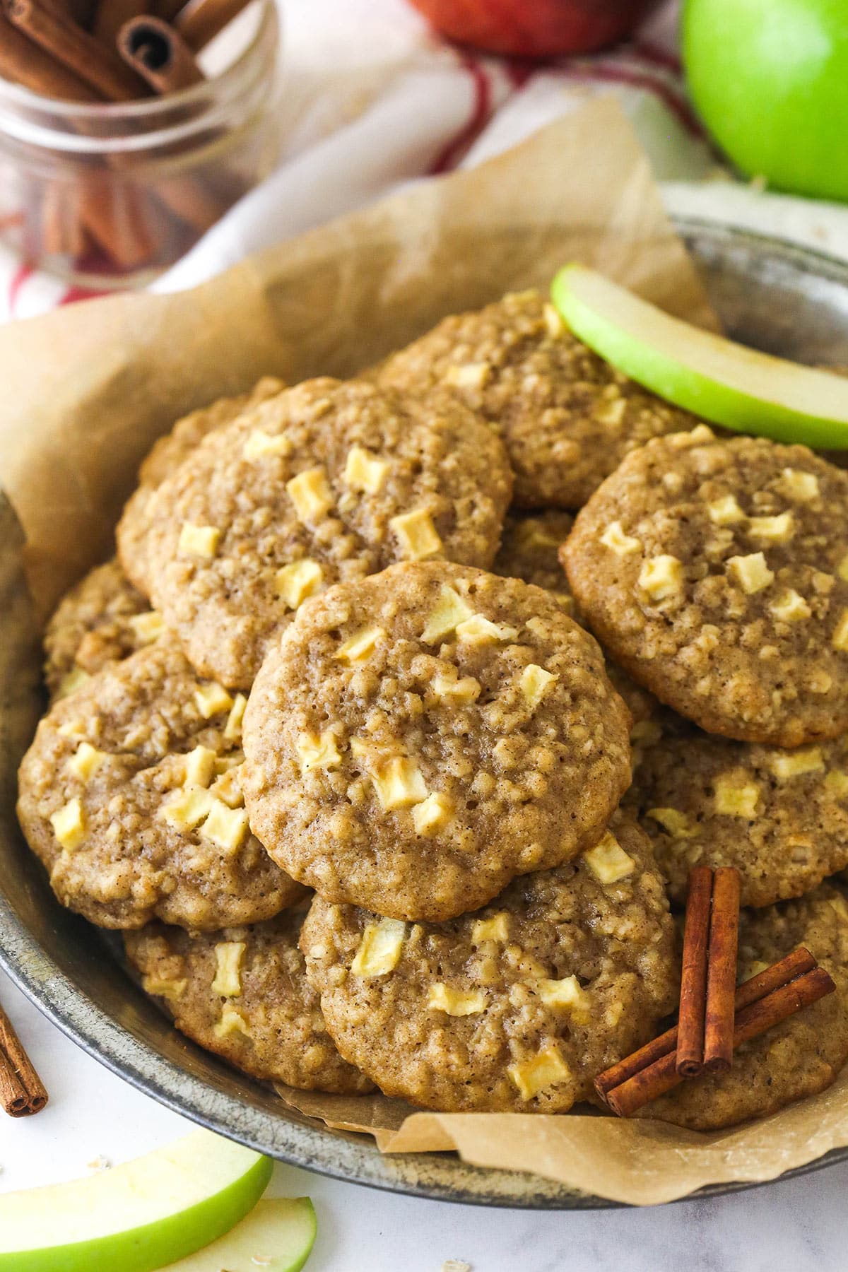 Apple Cinnamon Oatmeal Cookies baked on a lined baking sheet next to apples and cinnamon.