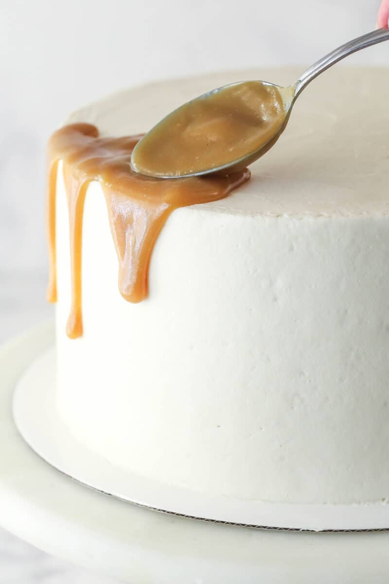 Spoon drizzling caramel around the outside of a cake.