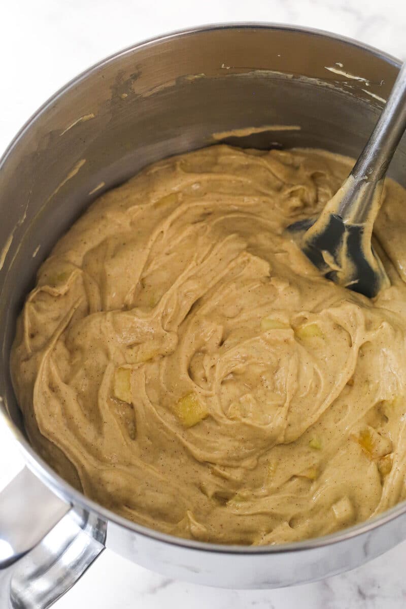 A mixing bowl filled with apple cake batter with a spatula sticking out.