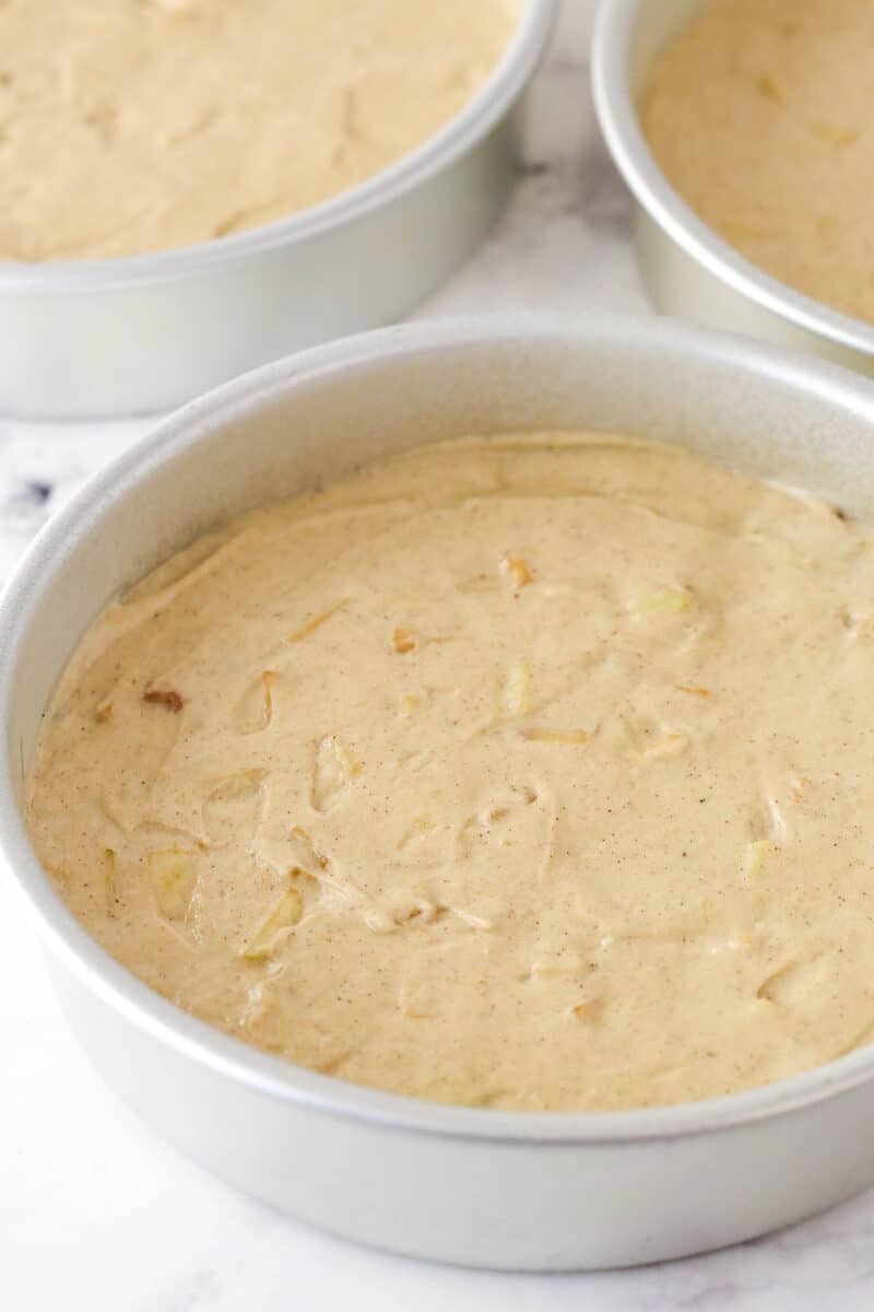 Three cake pans filled with apple cake batter.