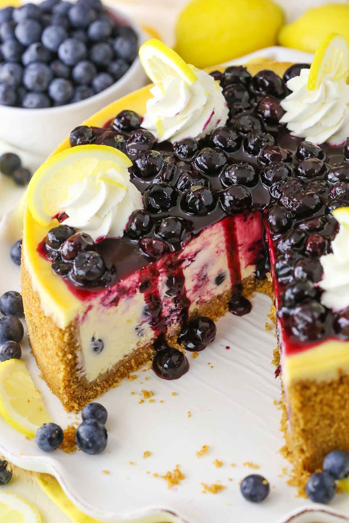 Overhead view of a Lemon Blueberry Cheesecake with a serving removed on a white cake stand