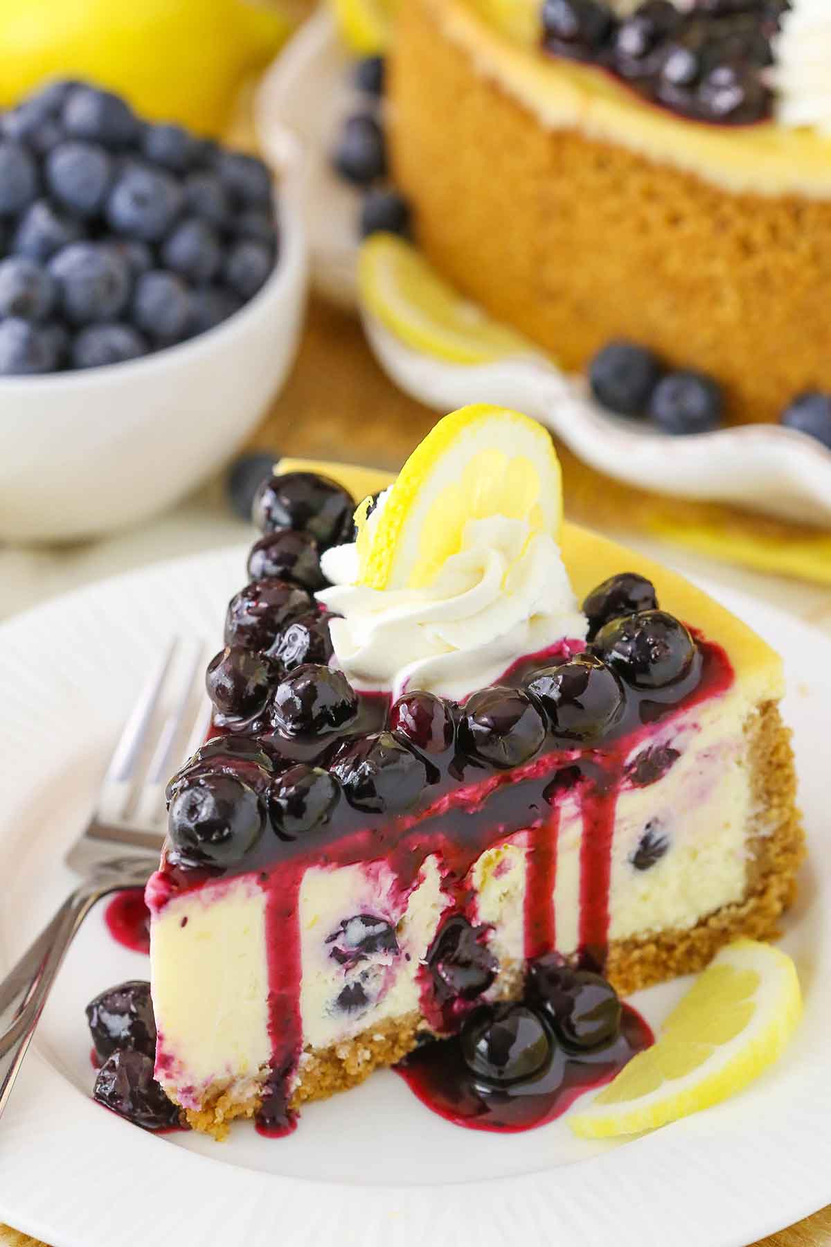 A slice of Lemon Blueberry Cheesecake next to a fork on a white plate