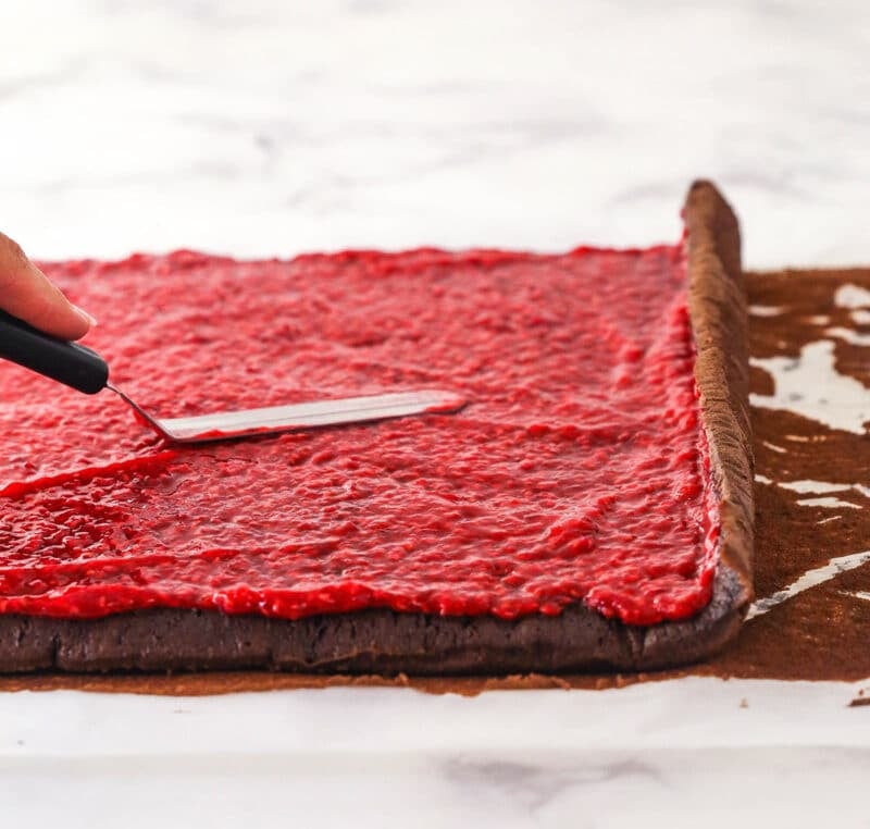 Raspberry sauce being spread on chocolate cake