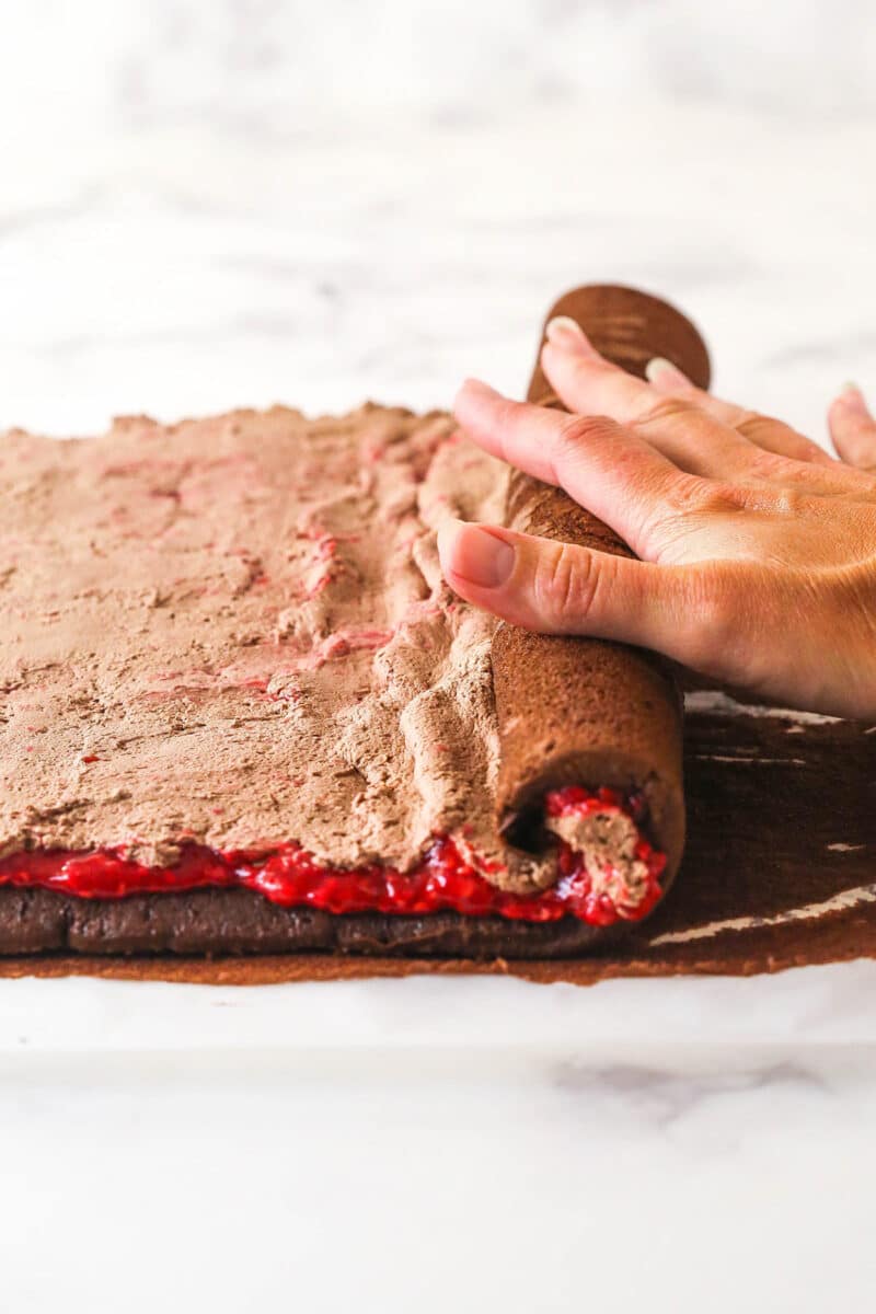 A hand rolling up raspberry chocolate cake roll