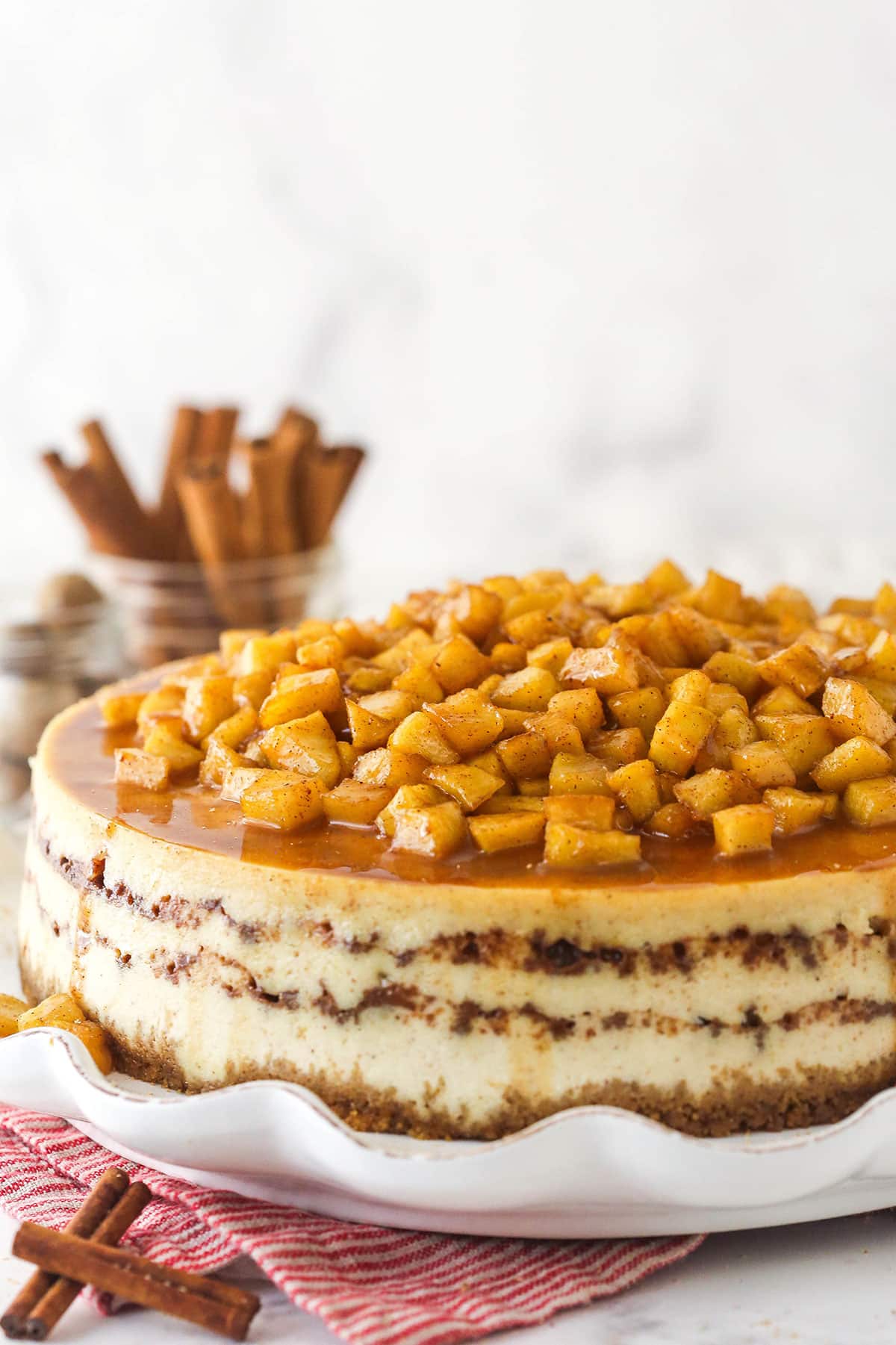 Side view of a whole Apple Cinnamon Cheesecake on a white serving plate.