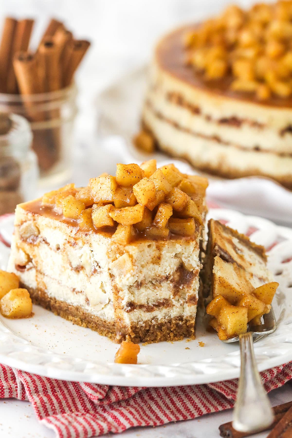 A slice of Apple Cinnamon Cheesecake on a small white plate with a fork holding a bite of cake.