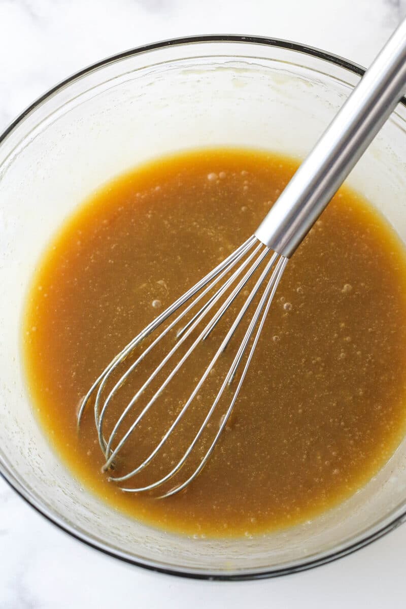 A mixture of butter and brown sugar in a glass mixing bowl with a metal whisk.