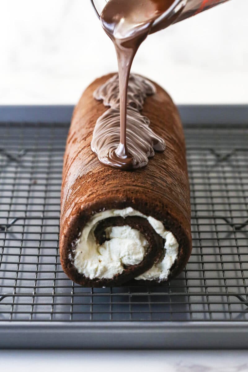 Chocolate glaze being poured over a chocolate roll cake