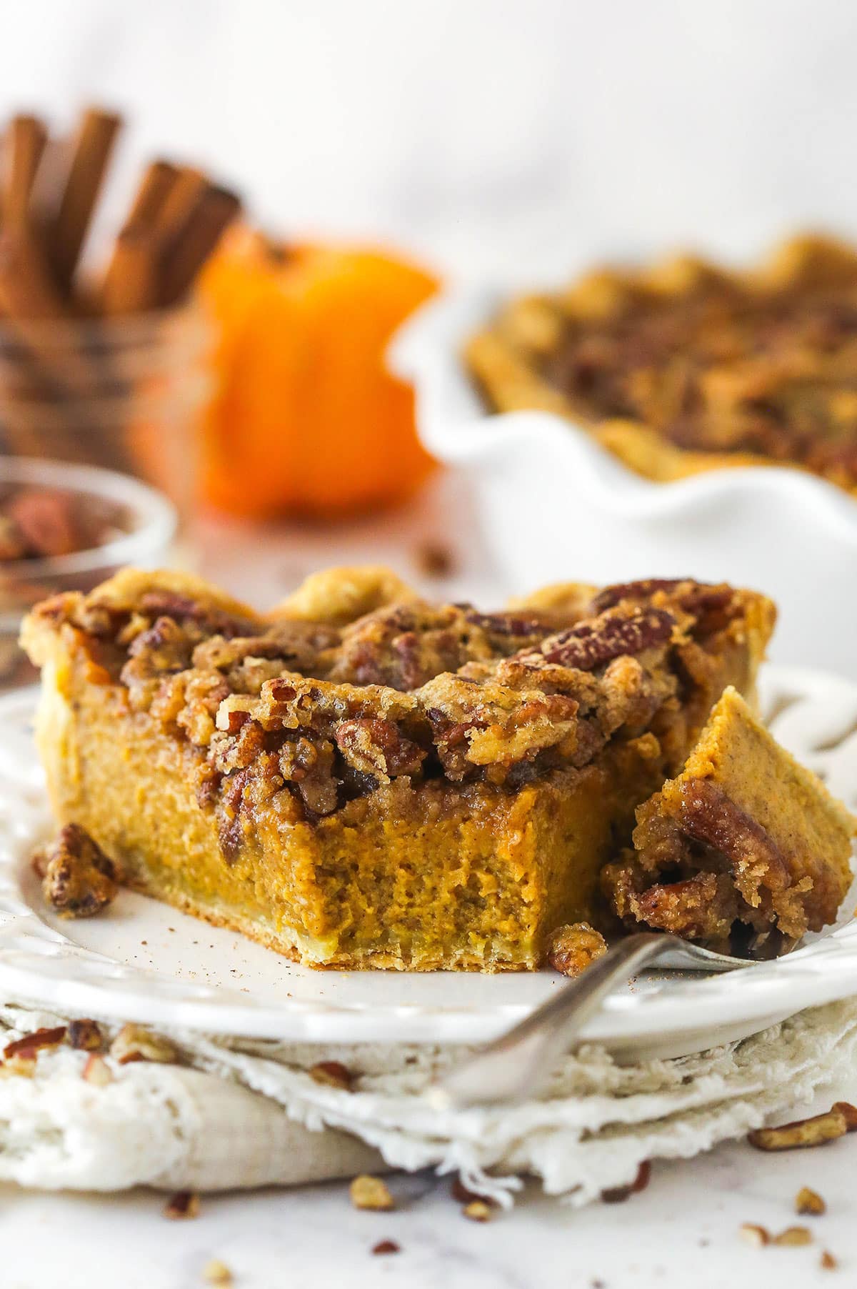 A slice of pecan praline pumpkin pie on a plate with a bite on a fork next to it.