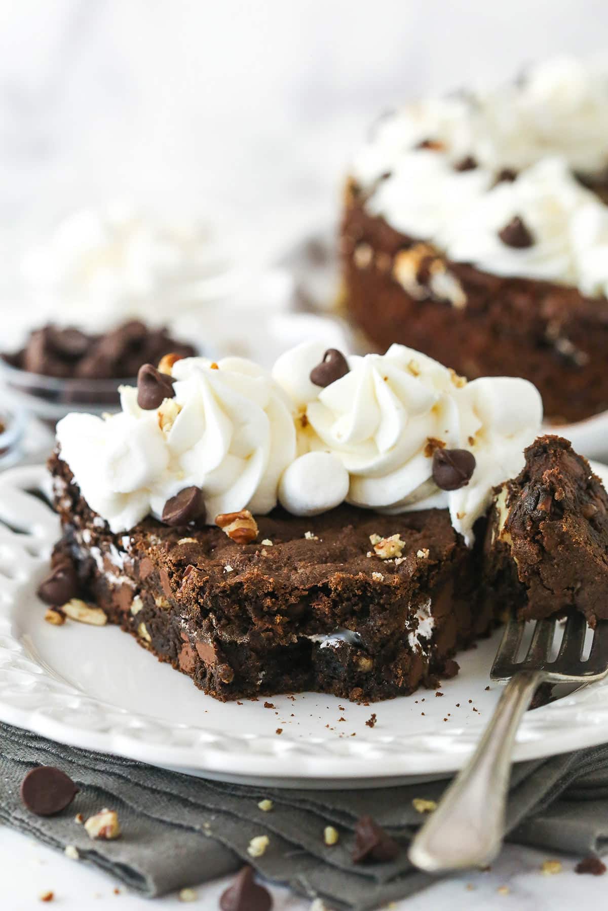 A slice of Rocky Road Cookie Cake on a small white plate with a bite removed on a fork.