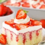 A square serving of Strawberry Poke Cake on a white plate next to a silver fork