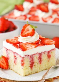 A square serving of Strawberry Poke Cake on a white plate next to a silver fork