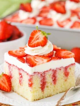 A square serving of Strawberry Poke Cake on a white plate next to a silver fork