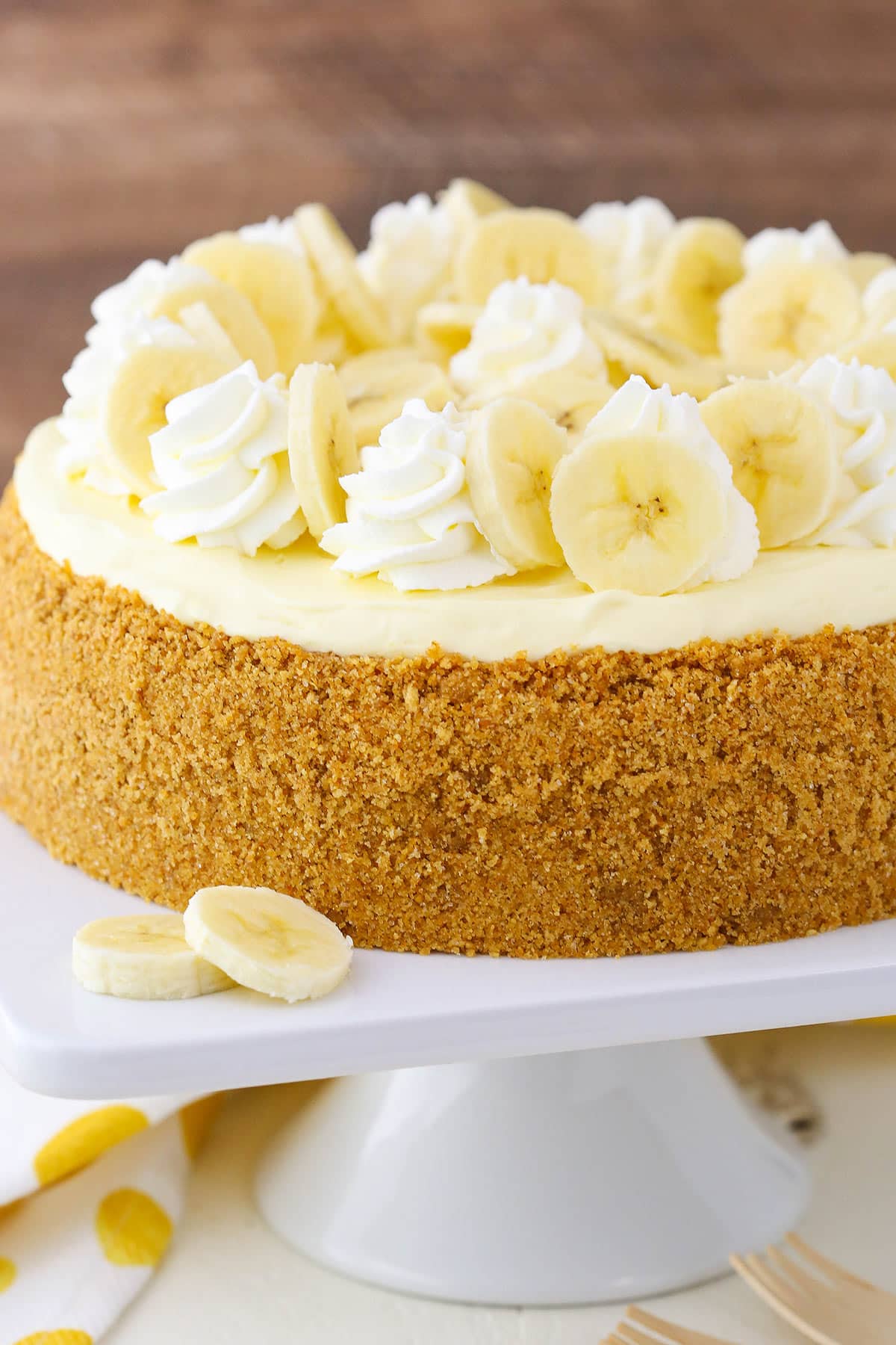 Side view of a full Banana Cream Cheesecake on a white cake stand