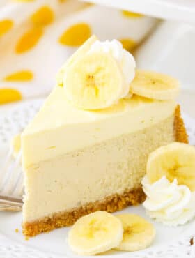 A slice of Banana Cream Cheesecake next to a fork on a white plate