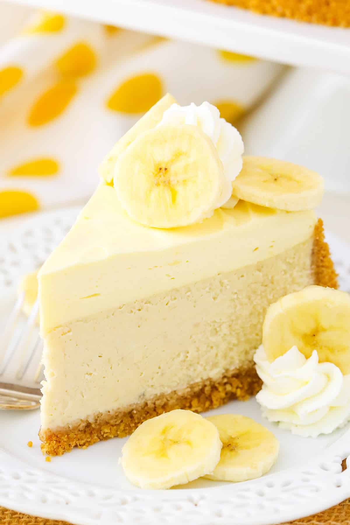 A slice of Banana Cream Cheesecake next to a fork on a white plate