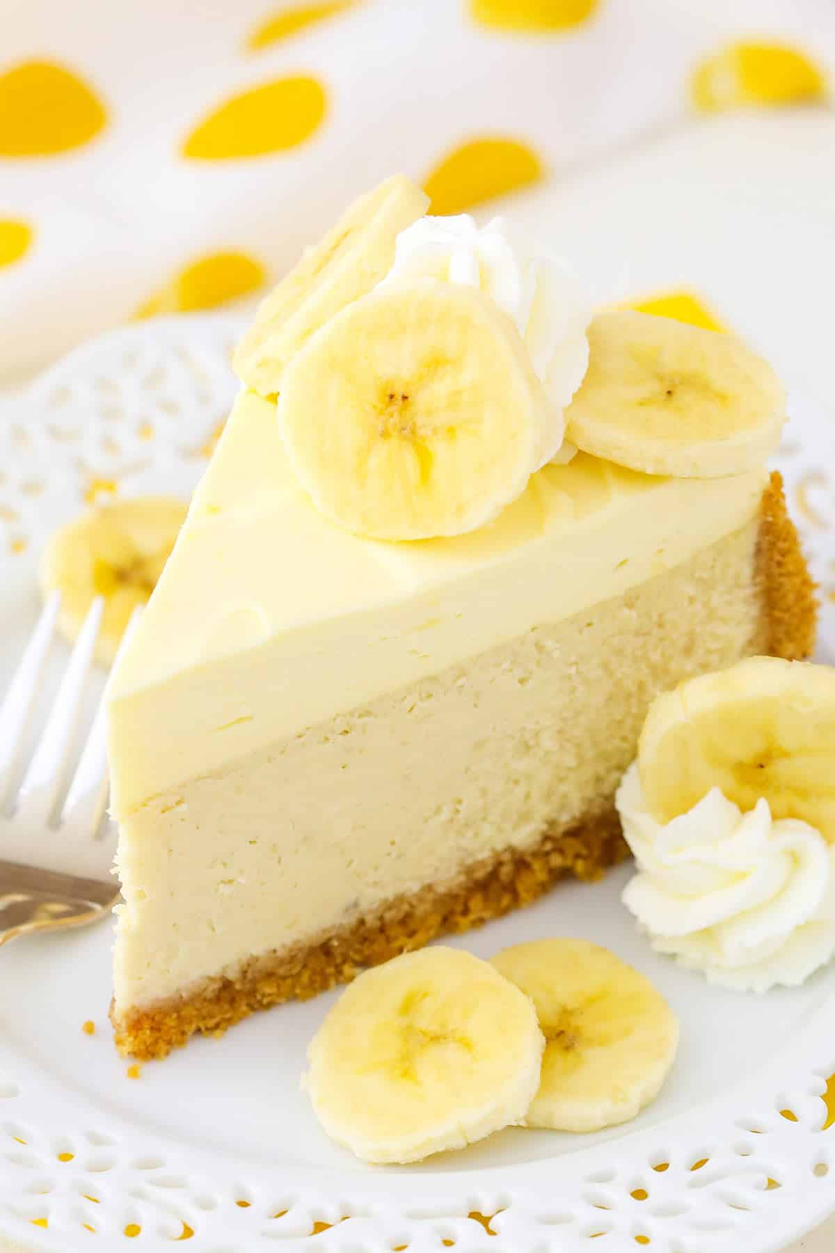 A slice of Banana Cream Cheesecake next to a fork on a white plate