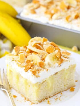 A square serving of Banana Poke Cake next to a fork on a white plate