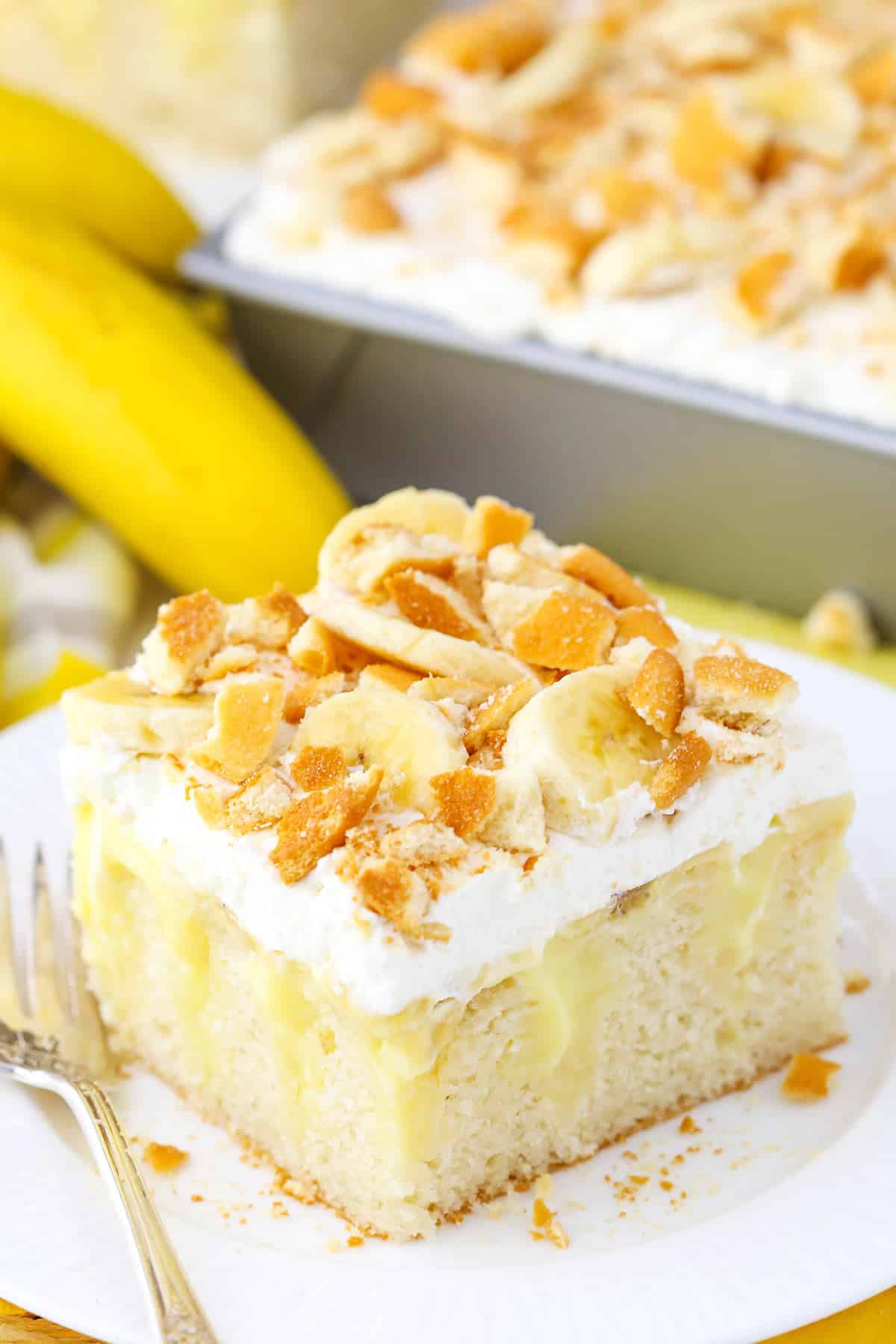 A square serving of Banana Poke Cake next to a fork on a white plate