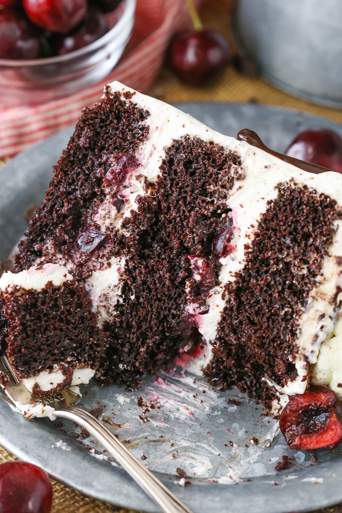 A slice of Black Forest Cake with a bite removed next to a silver fork on a gray plate