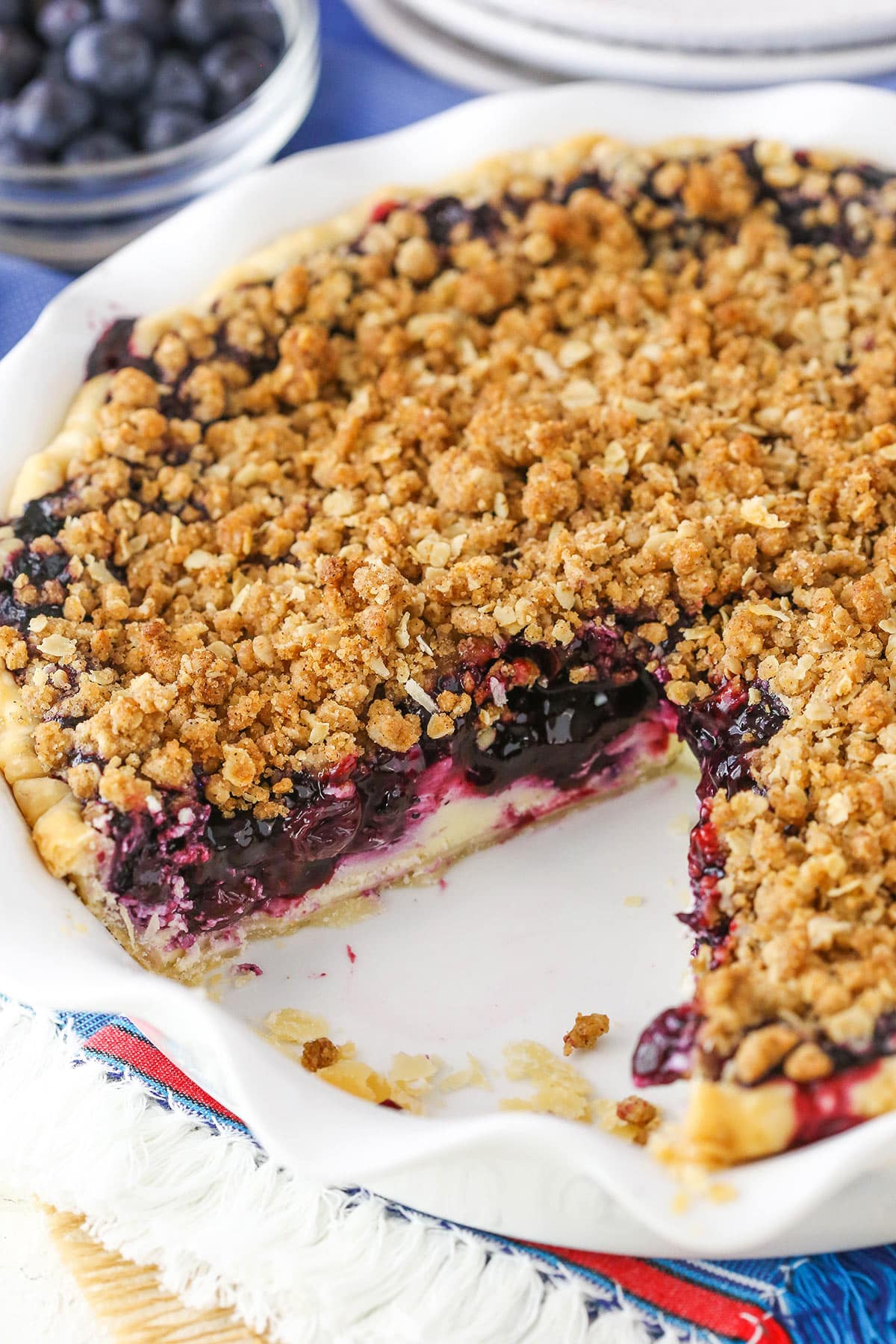 A Blueberry Crumb Cheesecake Pie with a slice removed in a white pie dish