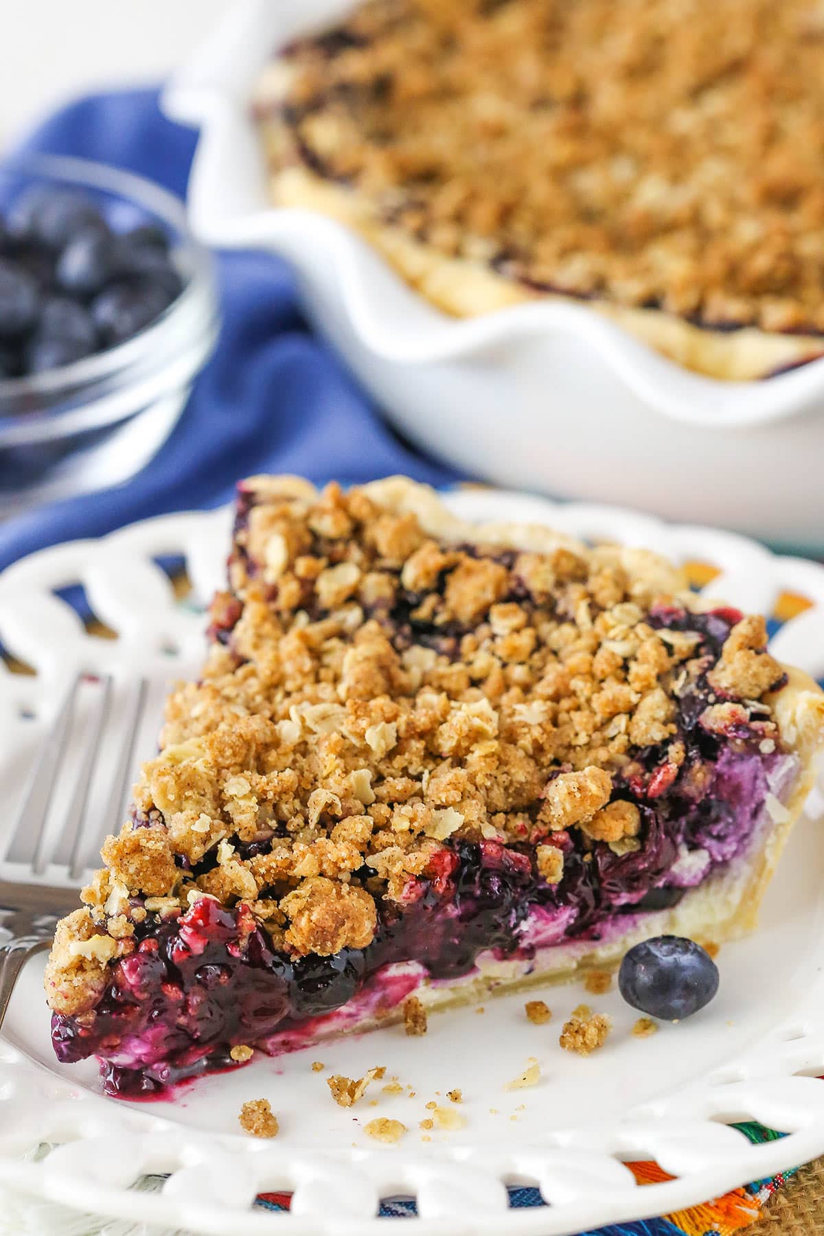 A slice of Blueberry Crumb Cheesecake Pie next to a fork on a white plate