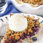 A slice of Blueberry Crumb Cheesecake Pie with a scoop of ice cream next to a fork on a white plate