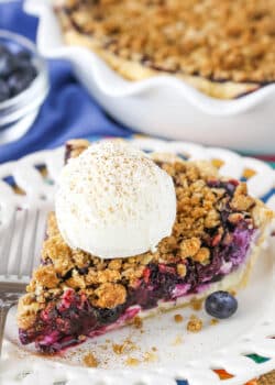 A slice of Blueberry Crumb Cheesecake Pie with a scoop of ice cream next to a fork on a white plate