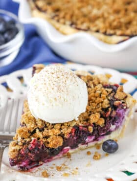 A slice of Blueberry Crumb Cheesecake Pie with a scoop of ice cream next to a fork on a white plate