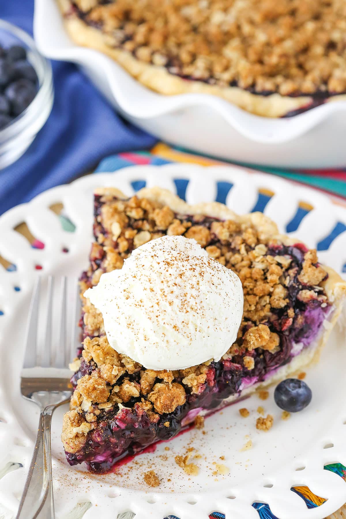 A slice of Blueberry Crumb Cheesecake Pie with a scoop of ice cream next to a fork on a white plate